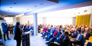 Een groep formeel-geklede mensen wordt aangesproken door de twee gastheren van de nieuwjaarsborrel